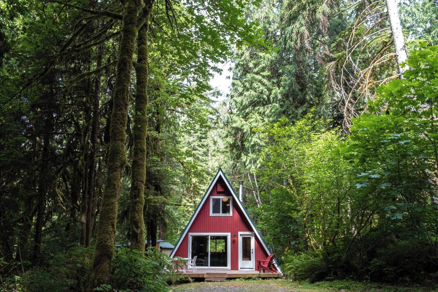 Una cabaña roja con techo triangular rodeada de un bosque denso.