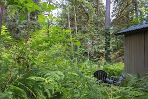 A forested area with a wooden structure, possibly a cabin, and a chair. - Forest A-Frame w/ Sauna | Dog Friendly | Mt Baker (Deming)
