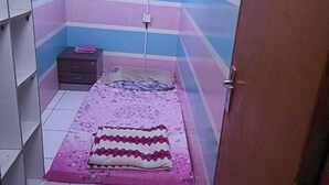A small, brightly colored room with a bed, a nightstand, and a wall-mounted shelf.