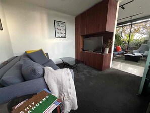 A modern living room with a grey sofa, a flat-screen TV, and a bookshelf. - Private balcony garden oasis in the heart of Fitzroy (Fitzroy)