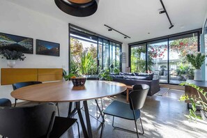 A modern interior with a round wooden table, black chairs, a dark blue sofa, and large windows offering a view of greenery. - Private balcony garden oasis in the heart of Fitzroy (Fitzroy)