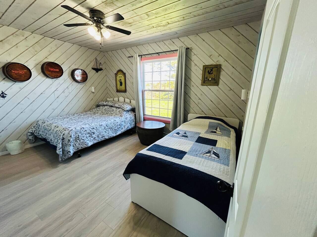 A bedroom with two beds, a ceiling fan, and a window with curtains.