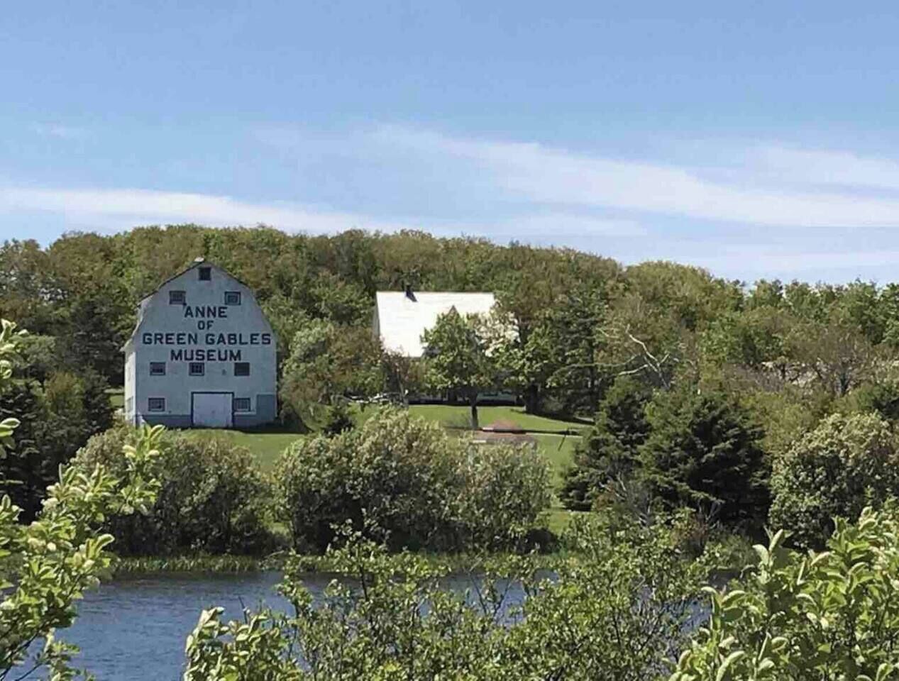 A white building with 'Anne of Green Gables Museum' written on it, surrounded by greenery and trees.