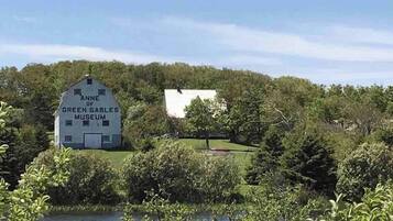 A white building with 'Anne of Green Gables Museum' written on it, surrounded by greenery and trees.