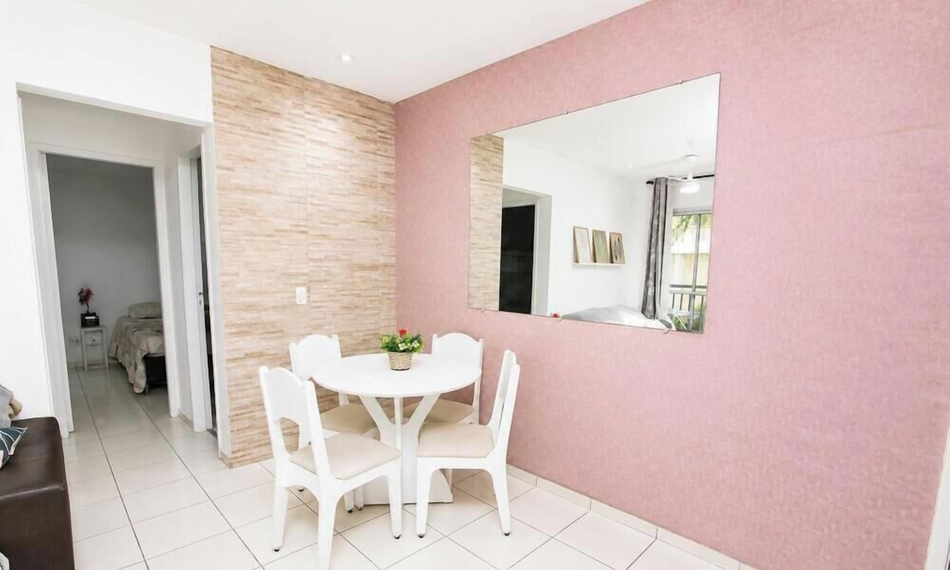 A dining area with a white table and chairs, a pink wall, and a large mirror.