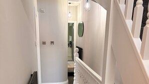 Um corredor com um radiador, um tapete estampado e um corrimão branco.