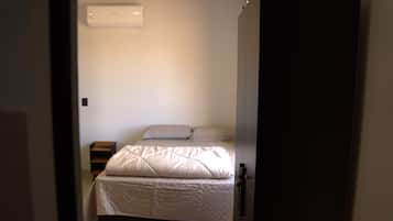Quarto com cama, mesa de cabeceira e ar condicionado fixado na parede.