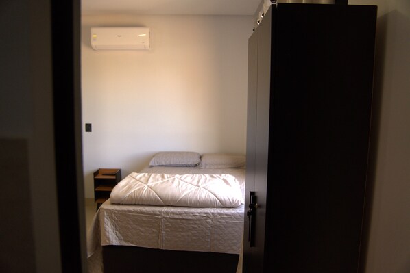 Une chambre à coucher avec un lit, une table de chevet et un climatiseur fixé au mur.