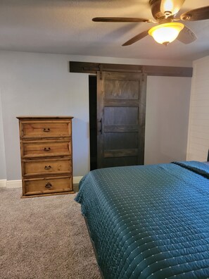 A bedroom with a bed, a dresser, a ceiling fan, and a door. - Spacious 4-bedroom house in Muskogee with AC (Muskogee)