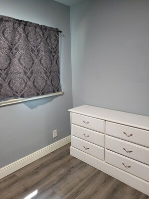 A room with a patterned curtain, a white dresser with drawers, and a wooden floor. - Spacious 4-bedroom house in Muskogee with AC (Muskogee)