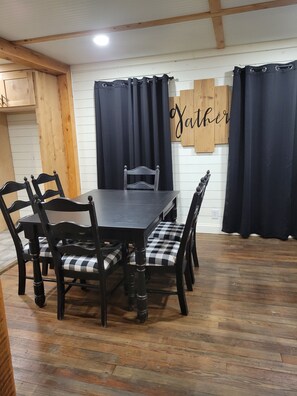A dining area with a wooden table and chairs, a black and white checkered cushion, and a 'Father' sign on the wall. - Spacious 4-bedroom house in Muskogee with AC (Muskogee)