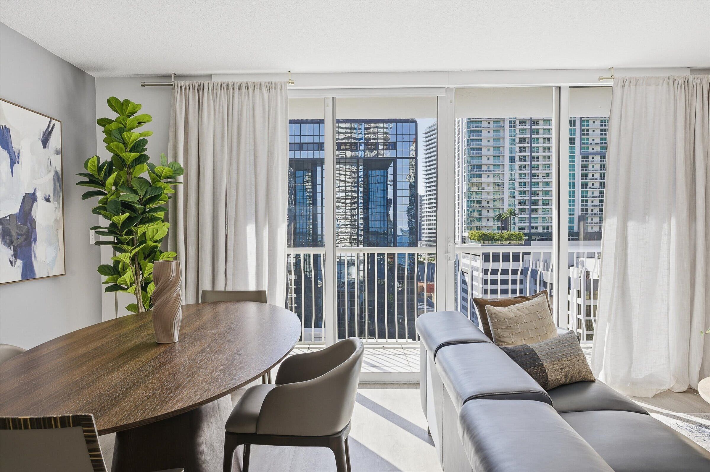 A modern living room with a dining table, sofa, and a balcony with a city view.