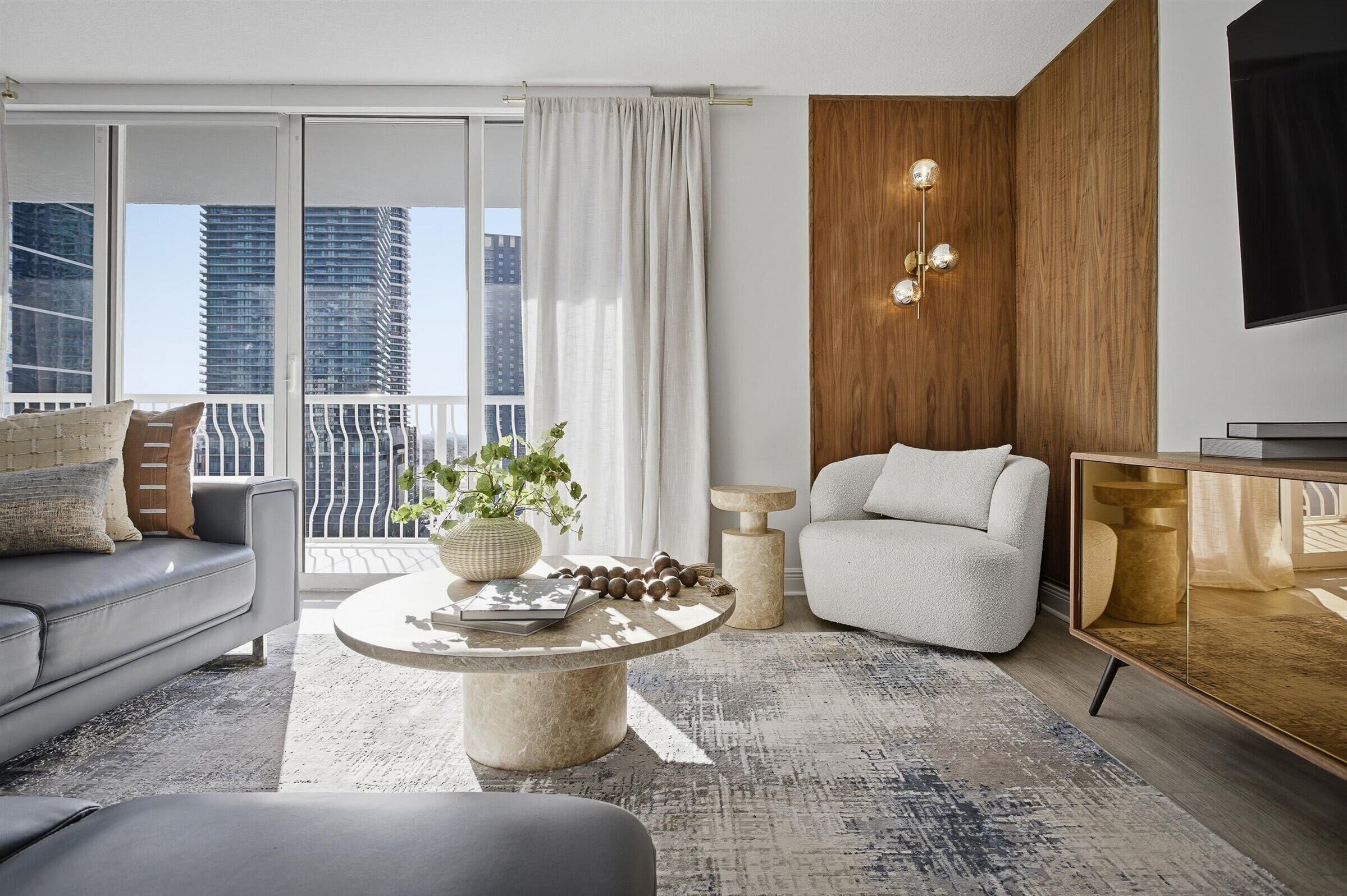 Una sala de estar moderna con un sofá, una mesa redonda de centro, una mesita auxiliar, una silla y un mueble para televisor.
