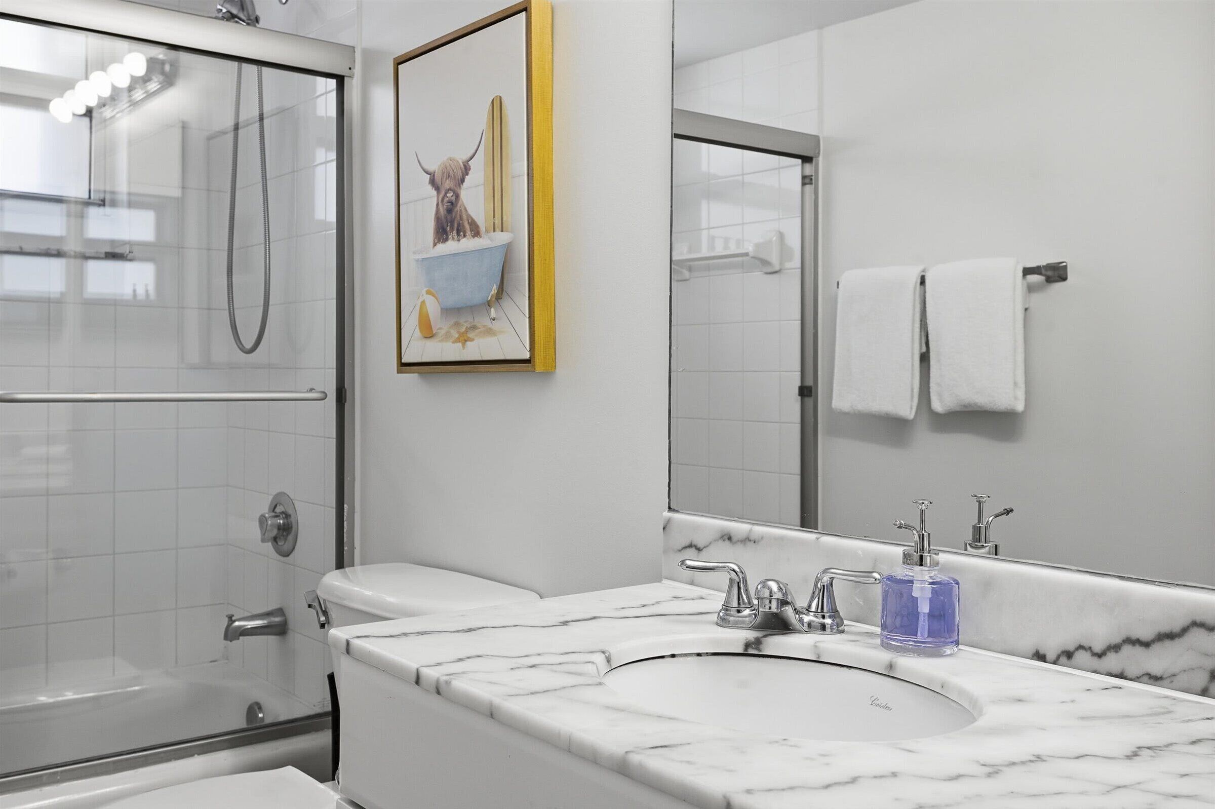 Un baño con cabina de ducha de vidrio, lavabo de mármol, un cuadro enmarcado de un perro y un perchero para toallas.