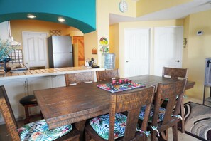 Un comedor con mesa y sillas de madera, una cocina al fondo y un dispensador de agua en la pared.