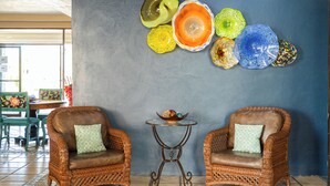 A room with two wicker armchairs, a small round table, and a wall decorated with colorful glass art. - Marina Pinacate B-302 (Puerto Peñasco)
