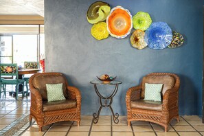 A room with two wicker armchairs, a small round table, and a wall decorated with colorful glass art. - Marina Pinacate B-302 (Puerto Peñasco)