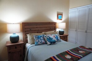 A bedroom with a wooden headboard, two bedside tables with lamps, a bed with a blue blanket and decorative pillows, and a wardrobe with louvered doors. - Marina Pinacate B-302 (Puerto Peñasco)