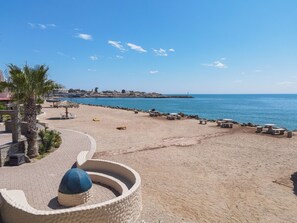 Une plage avec un muret en pierre, des chaises longues et un palmier.