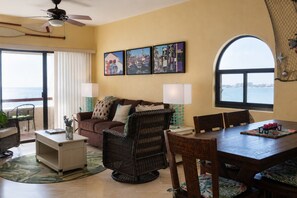 Un salon comprenant un canapé, une table à manger et des chaises, un ventilateur de plafond, et une vue sur la mer par une grande fenêtre.