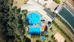 En vy från ovan av ett semesterområde med en swimmingpool, en tennisbana och en stor byggnad med ett sluttande tak.