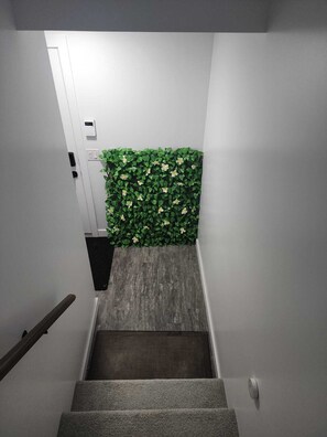 A staircase with a carpeted floor, a handrail, and a wall-mounted light switch. - A Place To Thrive. (Winnipeg)