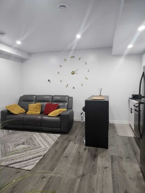 A modern living room with a black leather sofa, a patterned rug, and a kitchen area with a black countertop and white cabinets. - A Place To Thrive. (Winnipeg)