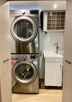 A compact laundry area with a stacked washer and dryer, a small sink, and a cabinet. - Modern 2BR Oasis Near Provenza (Medellín)