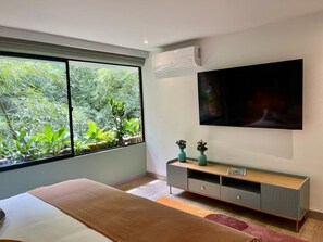 A modern bedroom with a large window, a bed, a TV mounted on the wall, and a minimalist console table. - Modern 2BR Oasis Near Provenza (Medellín)