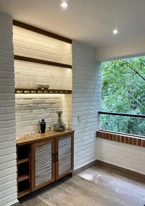 Une pièce d’angle avec un mur en briques blanches, un meuble en bois doté d’étagères et une fenêtre donnant sur la verdure.