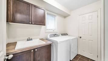 A laundry room with a sink, two washing machines, and wooden cabinets.