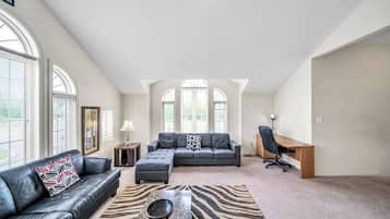 A spacious living room with a large grey sofa, a coffee table, and a desk with a chair.