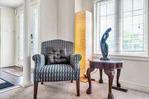 Un salon avec un fauteuil à motifs, un grand lampadaire et une sculpture décorative posée sur une table en bois.