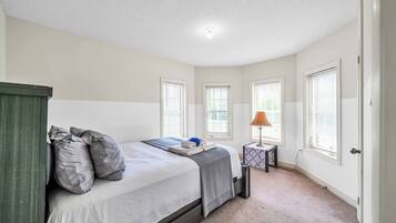 A bedroom with a bed, pillows, a bedside table with a lamp, and windows.