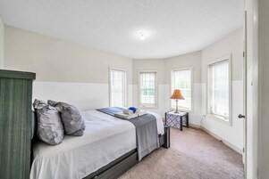 A bedroom with a bed, pillows, a bedside table with a lamp, and windows.