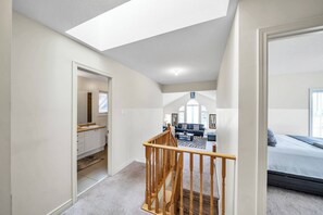 Amplio dormitorio tipo loft con un tragaluz grande, una zona de estar acogedora con sofá y mesa de centro, y un baño independiente con tocador y lavabo.