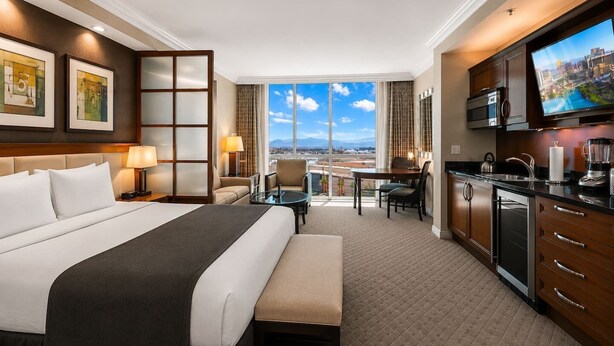 A hotel room with a large bed, a desk, a kitchenette, and a view of the city. - On LV Strip + Resort Access / Signature MGM (Las Vegas)