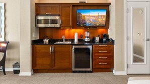 A compact kitchen with a microwave, toaster, and dishwasher. A flat-screen TV is mounted above the counter. - On LV Strip + Resort Access / Signature MGM (Las Vegas)