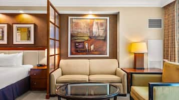 Une chambre d’hôtel avec un lit, un canapé, une table basse en verre, un tableau au mur et une lampe.