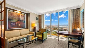 A hotel room with a sofa, armchair, coffee table, and a dining table. There is a large window with a view of the city. - On LV Strip + Resort Access / Signature MGM (Las Vegas)