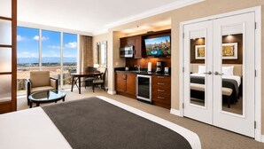 A hotel room with a large bed, a dining table with chairs, a kitchenette with a TV, and a view of the city. - On LV Strip + Resort Access / Signature MGM (Las Vegas)