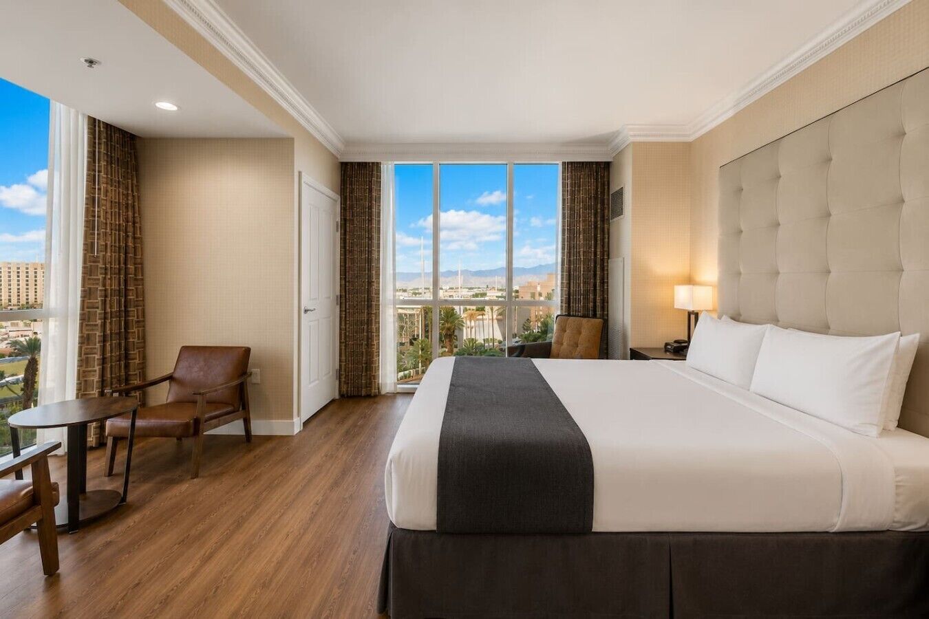 Une chambre d’hôtel avec un grand lit, une chaise, une petite table et une vue sur le paysage urbain par la fenêtre.