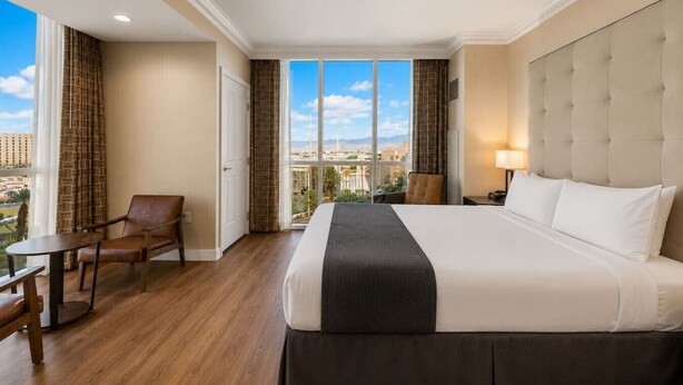 Ein Hotelzimmer mit einem großen Bett, einem Sessel, einem kleinen Tisch und Blick auf die Stadt.