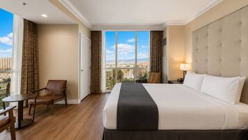 Une chambre d’hôtel avec un grand lit, une chaise, une petite table et une vue sur le paysage urbain par la fenêtre.