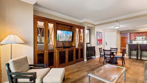 Ein modernes Wohnzimmer mit Flachbildfernseher, Holzsärchen, einer Essecke mit Stühlen und einer Küche im Hintergrund.