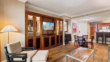 Un salon moderne doté d’un téléviseur à écran plat, de meubles en bois, d’un coin repas avec des chaises et d’une cuisine en arrière-plan.