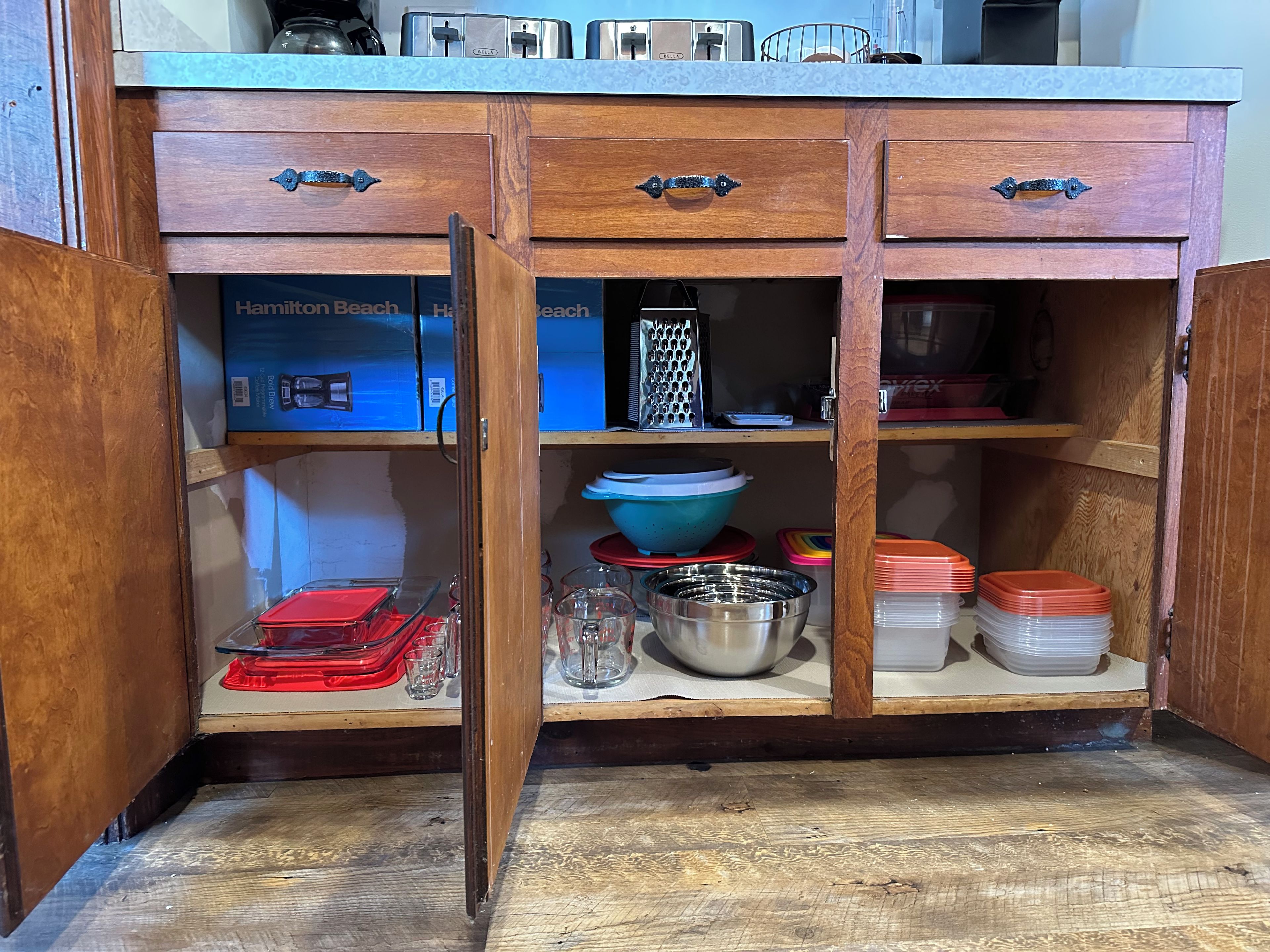 A kitchen with wooden cabinets, a countertop, and various kitchenware including bowls, plates, and a grater.
