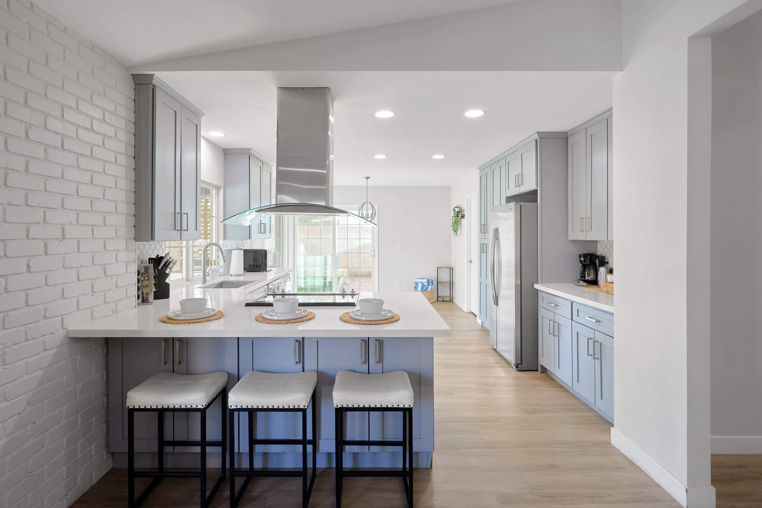 A modern kitchen with a central island, bar stools, and a view to the outdoors.