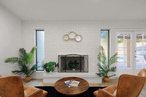 A room with a white brick fireplace, two potted plants, a round wooden coffee table with magazines, and leather armchairs. - Sunnyside - Pool - Putting Green - Game Room (Phoenix)