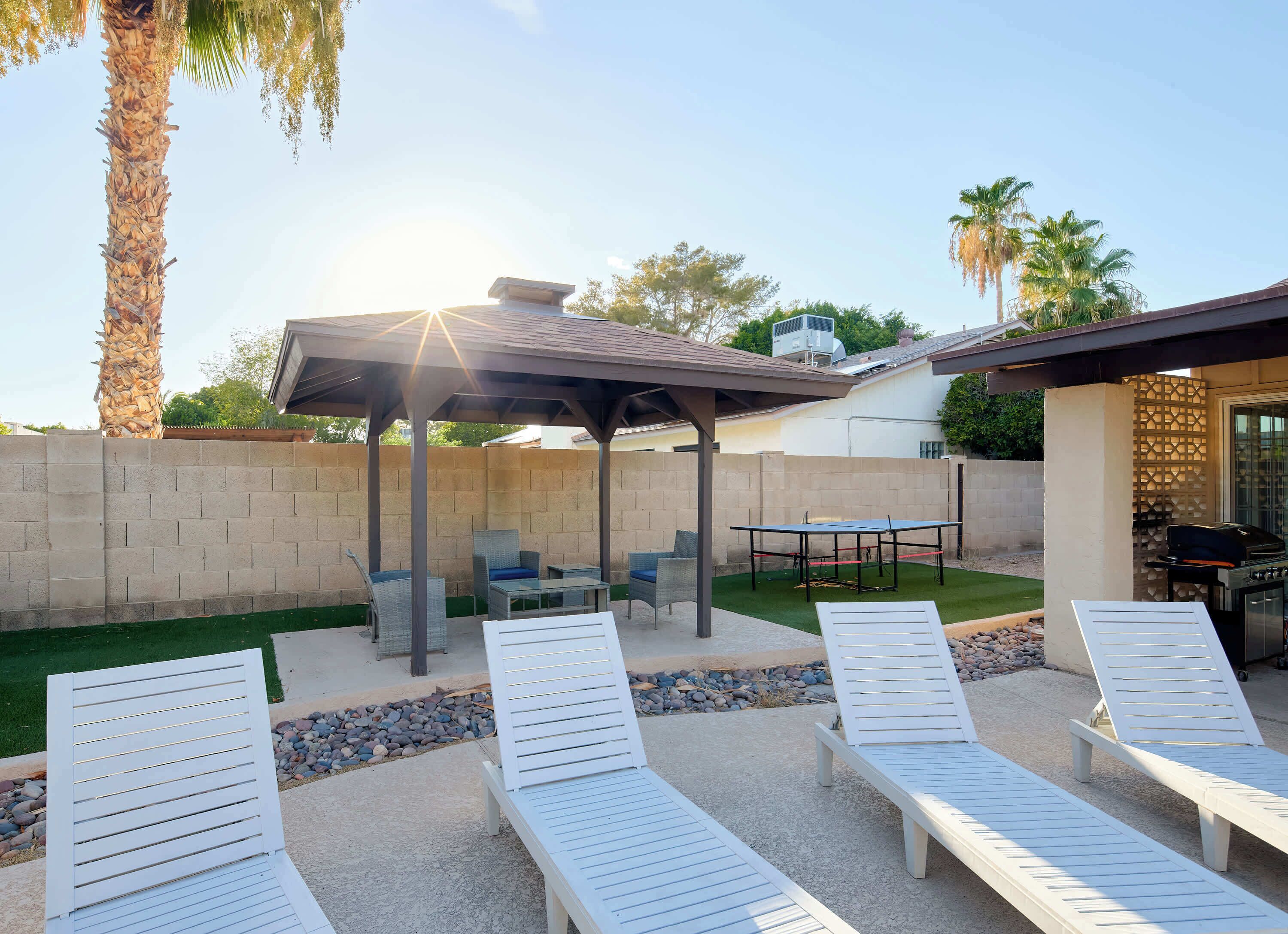A covered outdoor seating area with lounge chairs, a table, and a grill.